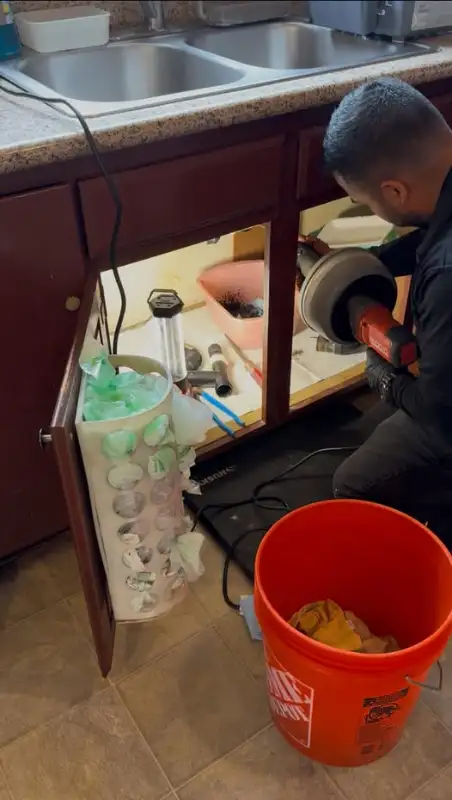 Plumber running a drain snake under a kitchen sink