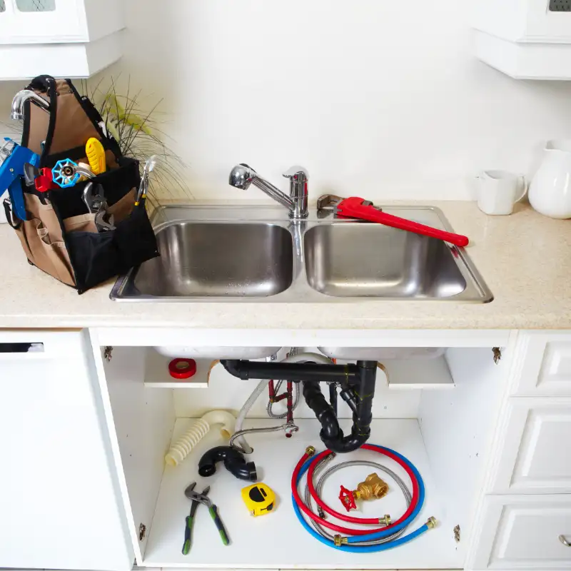 Open cabinet under a kitchen sink with new drain parts and supply hoses