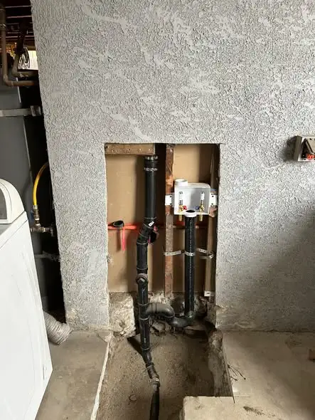 Opened wall showing new black drain lines and a washer box