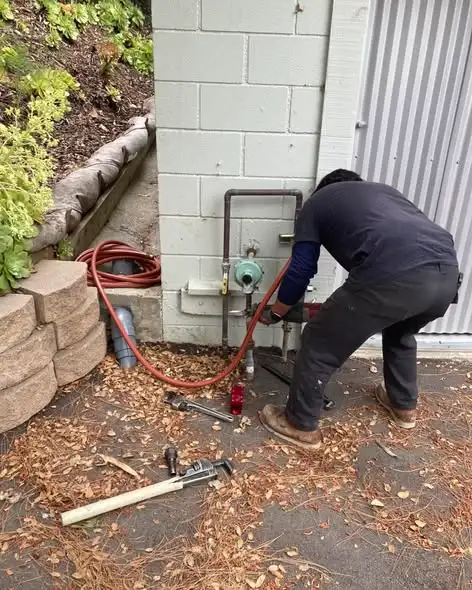 Plumber repairing an outdoor water line beside a house
